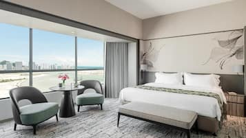 A hotel room with a large window, a bed, a round table, two chairs, and a bench.