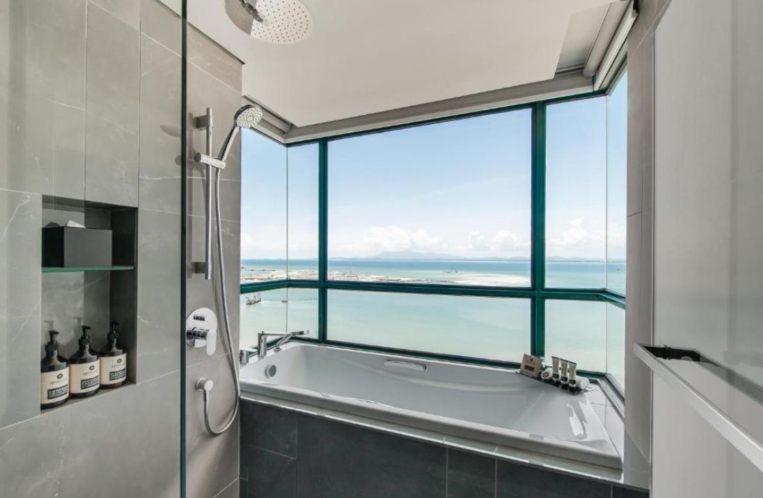 A modern bathroom with a large bathtub, a glass-enclosed shower, and a view of the sea.