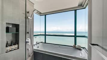 A modern bathroom with a large bathtub, a glass-enclosed shower, and a view of the sea.