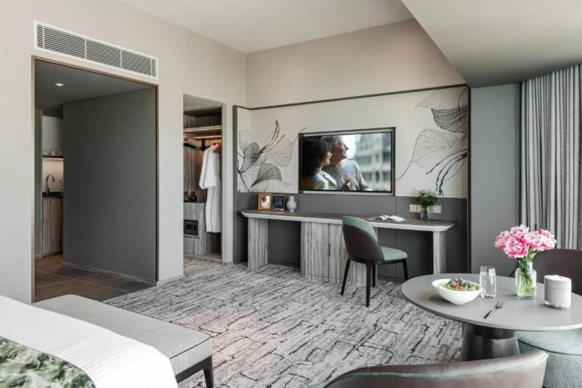 A modern hotel room with a dining area, a TV mounted on the wall, and a visible closet.