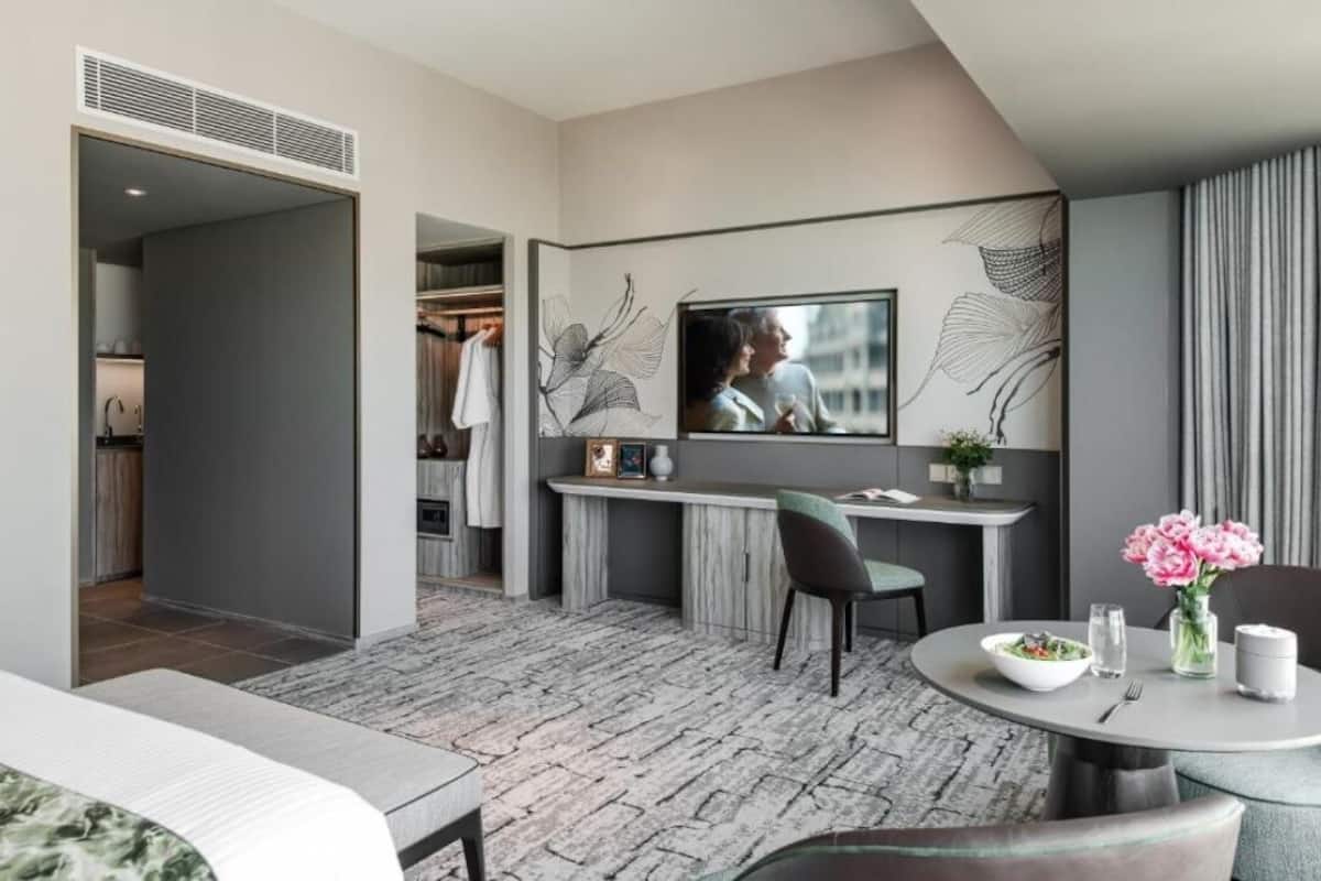 Una habitación de hotel moderna con zona de comedor, televisor montado en la pared y un armario visible.