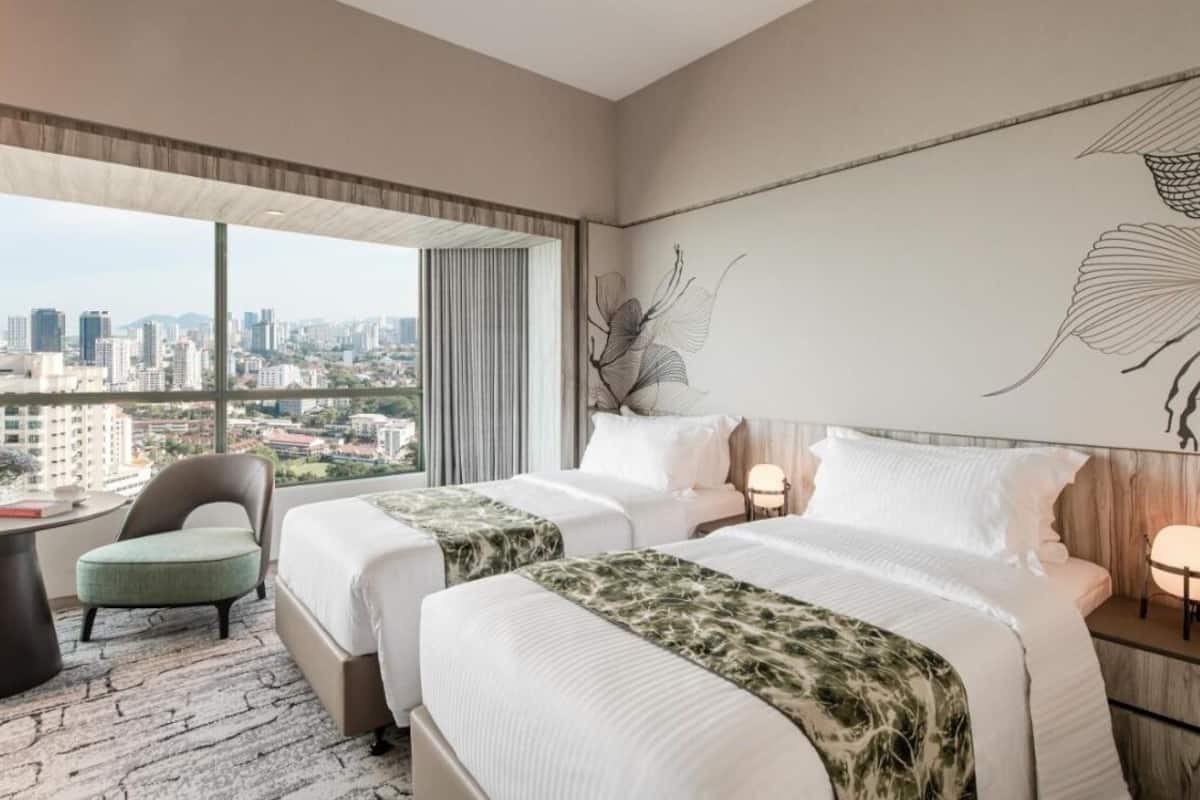 Habitación de hotel con dos camas, vistas a la ciudad, un cuadro abstracto grande y un paisaje urbano visible a través de la ventana.