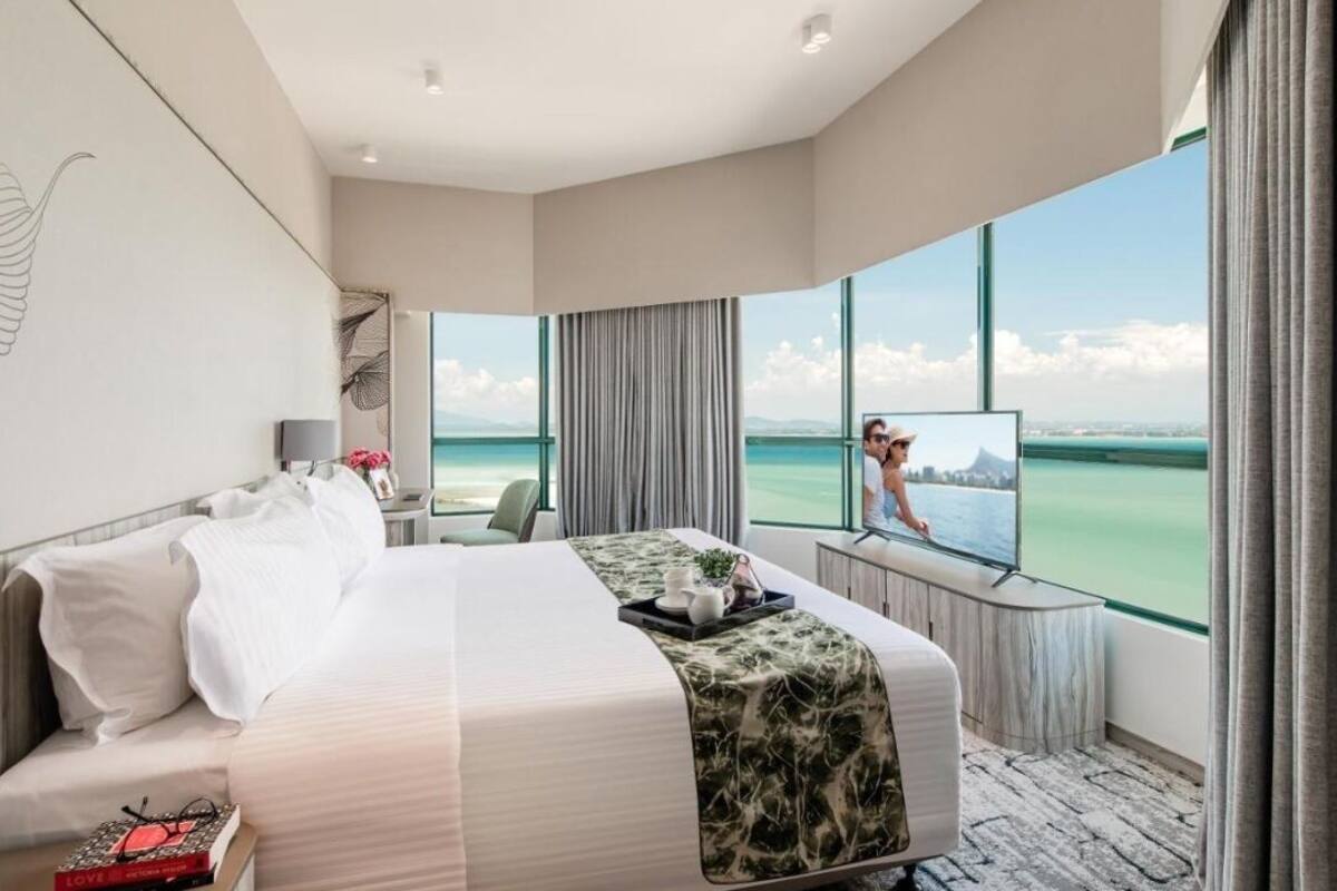 A hotel room with a large bed, a desk, a TV, and a view of the ocean.