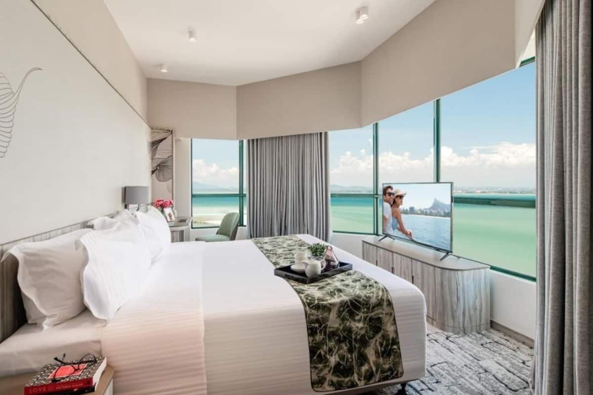 Habitación de hotel con una cama grande, un escritorio, un televisor y vista al océano.