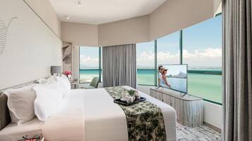 A hotel room with a large bed, a desk, a TV, and a view of the ocean.