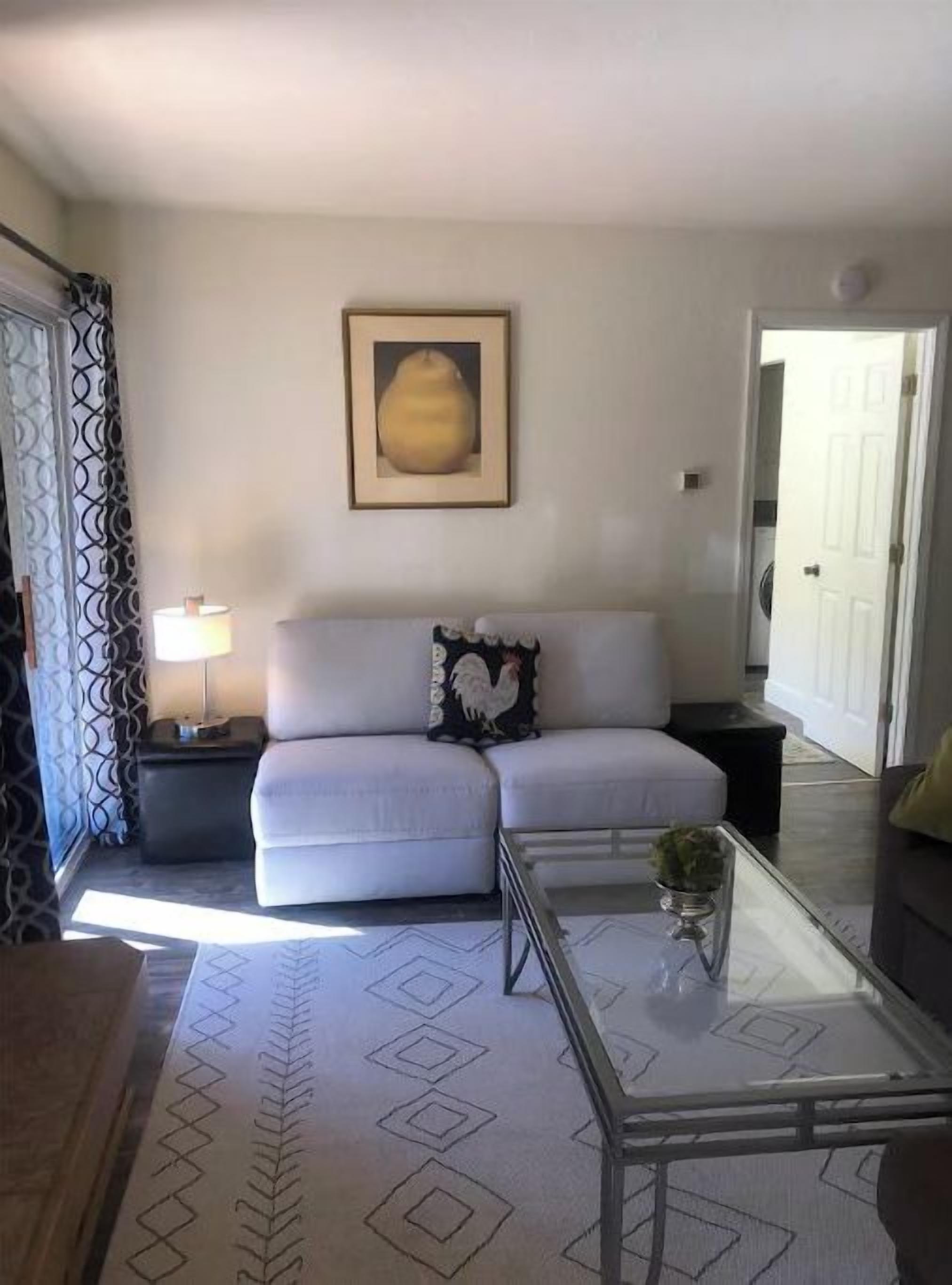 A living room with a white sofa, a glass coffee table, a patterned rug, and a framed picture on the wall.