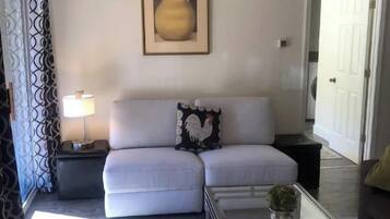 A living room with a white sofa, a glass coffee table, a patterned rug, and a framed picture on the wall.