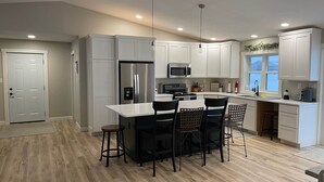 Una cocina moderna con armarios blancos, un refrigerador de acero inoxidable, un microondas y un comedor con sillas negras.