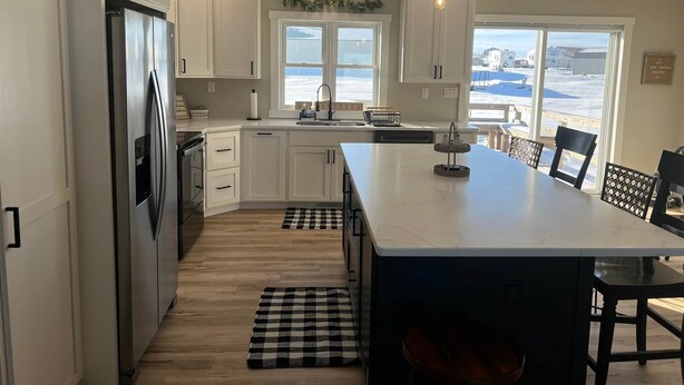 Una cocina moderna con armarios blancos, un refrigerador de acero inoxidable, una isla grande y vistas a la playa a través de las ventanas.