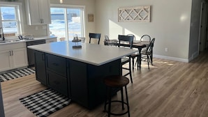 Una cocina moderna con una isla grande, armarios blancos y un comedor con mesa y sillas.