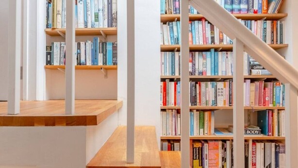 A staircase with wooden steps and white railings leading to a bookshelf filled with books. - Cosy 1 Bedroom Apartment Near Wimbledon Station (London)