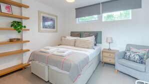 A modern bedroom with a bed, bedside tables, a sofa, and a window with blinds. - Cosy 1 Bedroom Apartment Near Wimbledon Station (London)