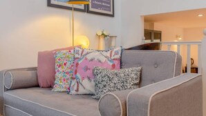 A grey sofa with floral and patterned cushions, a floor lamp, and framed artwork on the wall. - Cosy 1 Bedroom Apartment Near Wimbledon Station (London)