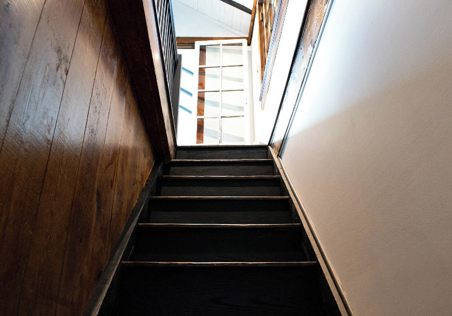 A wooden staircase leading to a room with a white wall and a window.