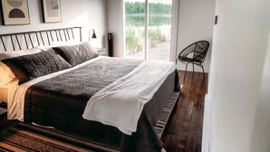 Ein Schlafzimmer mit einem großen Bett, einem Sessel und Seeblick durch eine Glastür.