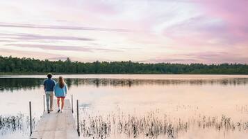 A couple standing on a wooden dock extending into a calm lake, with a forested shoreline in the background.