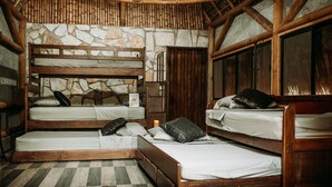 A rustic room with a stone wall, wooden beds, and a checkered floor. - Selva Teenek (Ciudad Valles)