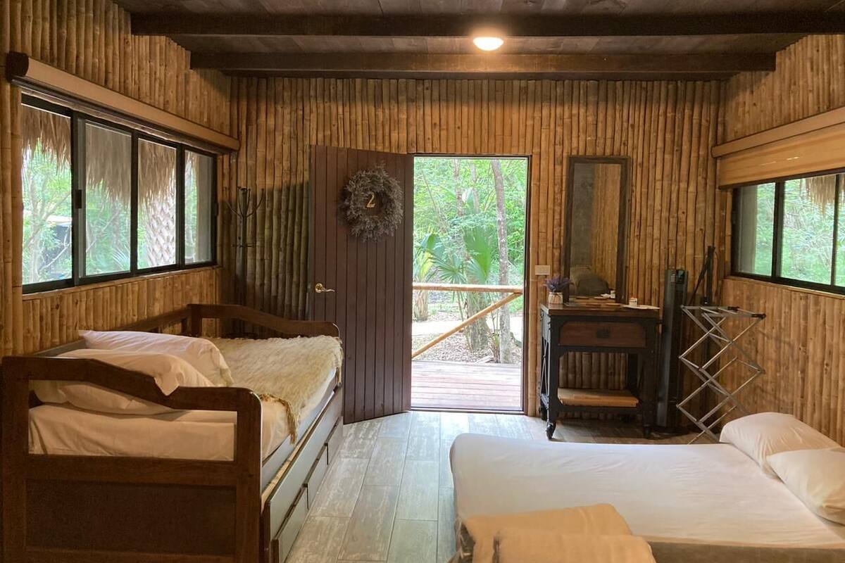 A cabin-style room with two wooden beds, a desk, and a view of the outdoors.