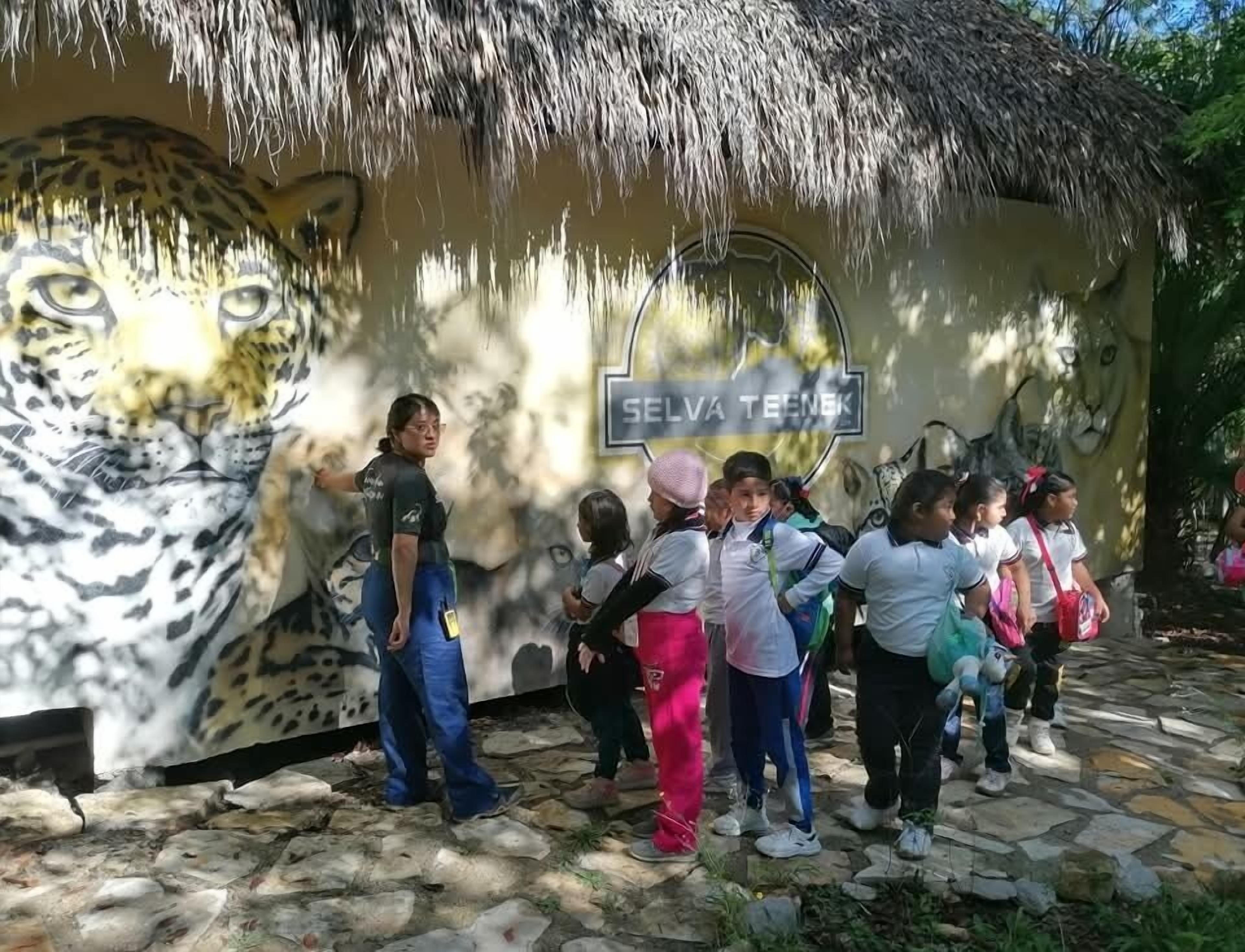 Un grupo de niños posa frente a un mural con un leopardo enorme y un letrero que dice "SELVA TEENK".