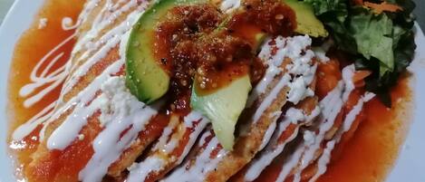 A plate of enchiladas topped with avocado, sour cream, and a red sauce, accompanied by a side salad.