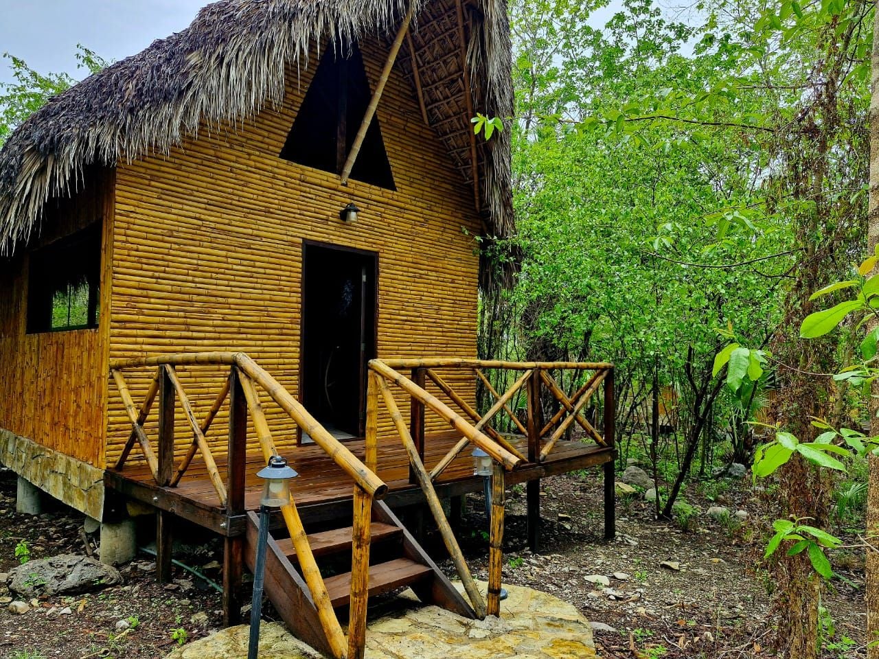 A wooden cabin with a thatched roof, a wooden deck, and a staircase leading to the entrance.