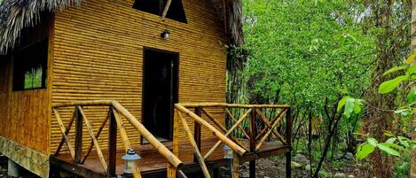 A wooden cabin with a thatched roof, a wooden deck, and a staircase leading to the entrance.