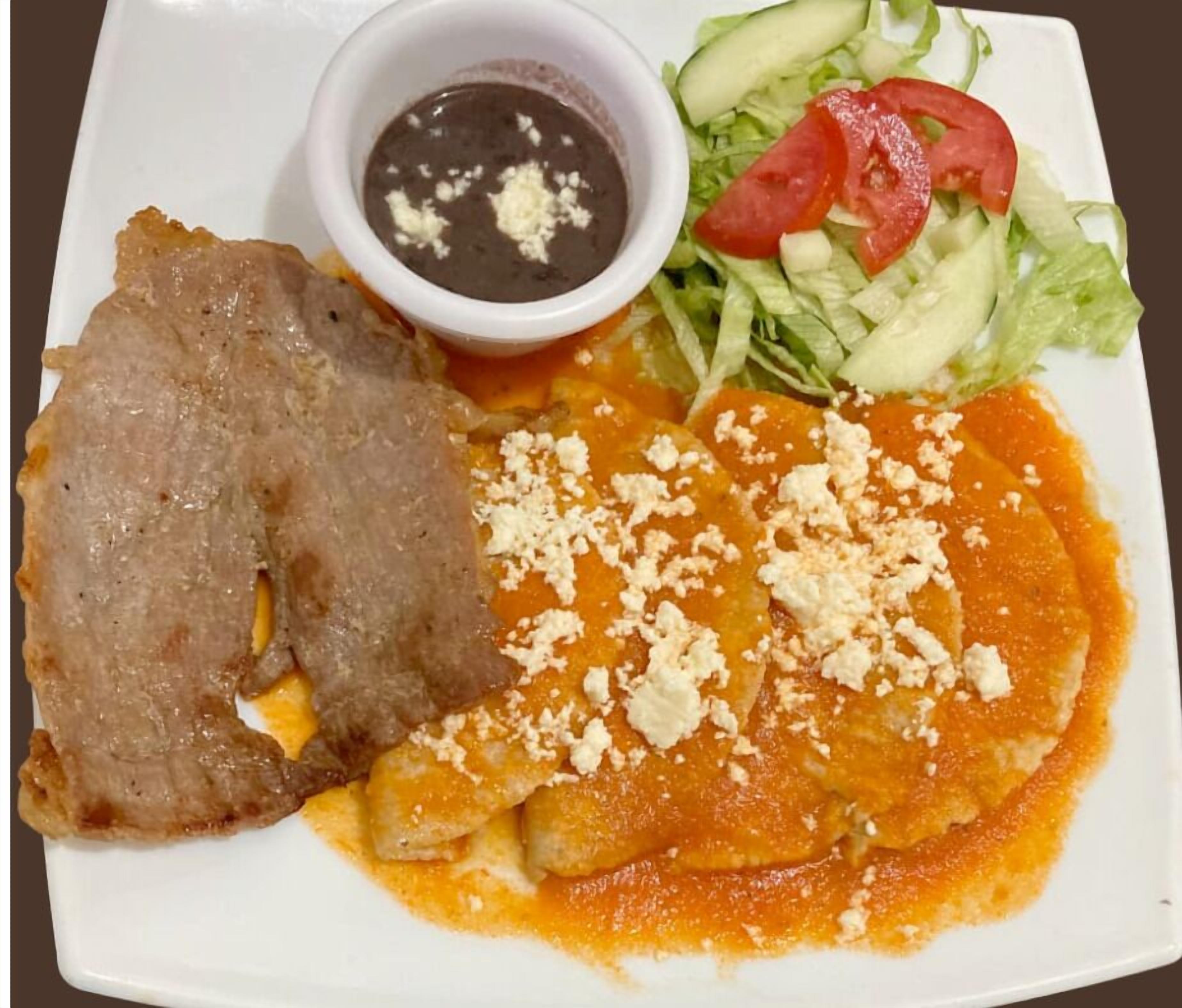 Un plato con un guiso de carne, un bol de salsa y una ensalada.