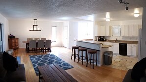 Amplia sala de estar con una mesa de comedor de madera, una cocina con armarios blancos y una pequeña barra.