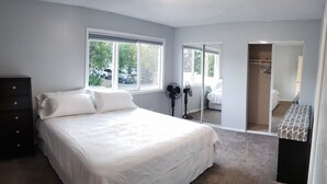 Un dormitorio con una cama grande, un aparador, un ventilador y un vestidor.