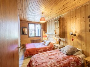 Ein Zimmer in einer Holzhütte mit zwei Betten, einem Fenster, einem Spiegel und einer Wandlampe.