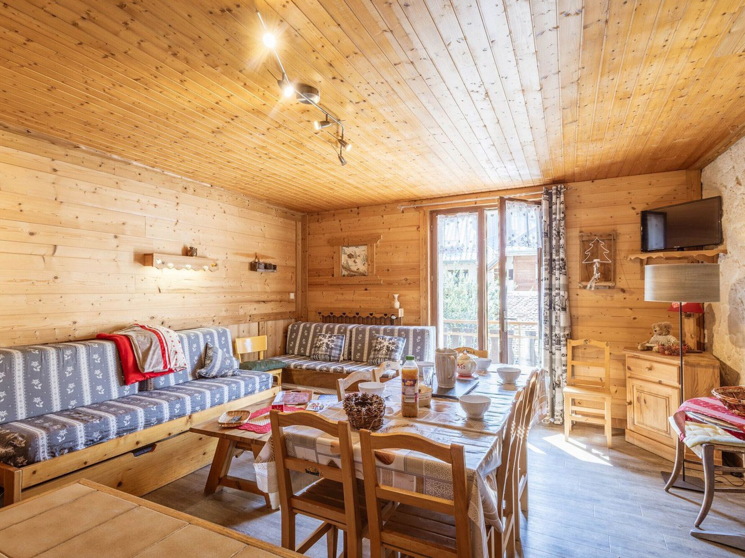 Ein gemütliches Blockhaus-Interieur mit Holzbalkendecke, einer Couch, einem Esstisch und einem an der Wand befestigten Fernseher.