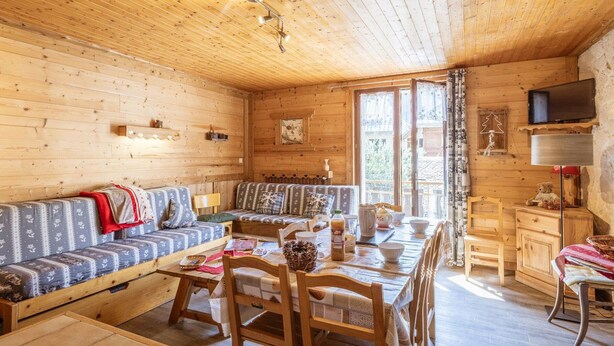 A cozy cabin interior with a wooden ceiling, a sofa, a dining table, and a television mounted on the wall. - Spacious apartment, pets allowed - 8 guests (Valloire)