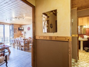 A room with a wooden ceiling, a dining area with chairs and a table, a wall-mounted mirror, and a bathroom with a sink and tiled floor.