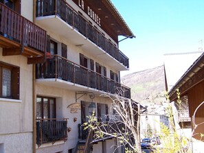 Ein mehrstöckiges Gebäude mit Balkonen, einem Schild, das ein Restaurant anzeigt, und Blick auf eine gebirgige Landschaft.