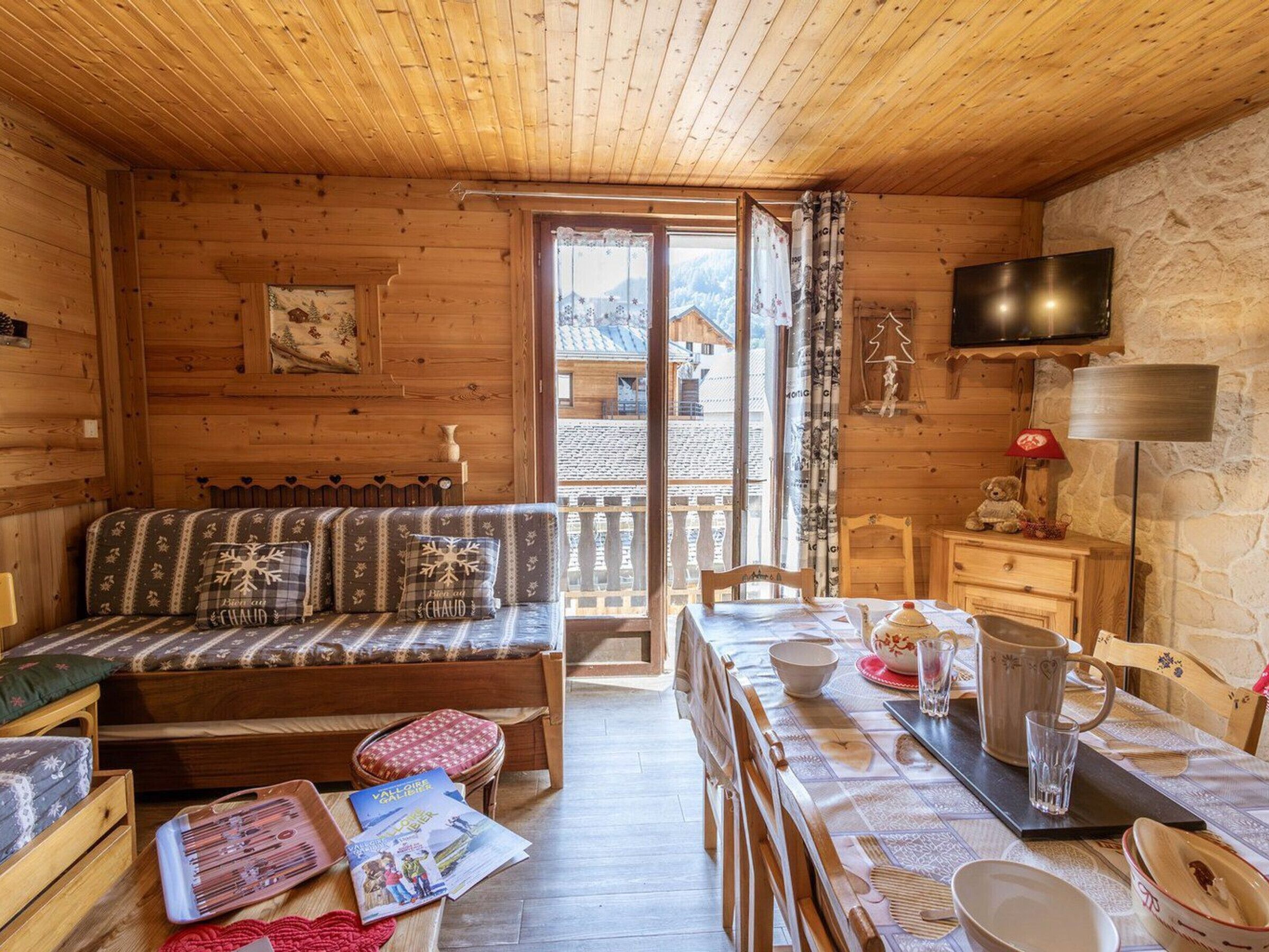 A cozy wooden cabin with a sofa, dining table, and a TV mounted on the wall.