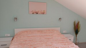 Une chambre à coucher comprenant un lit, une table de chevet, une lampe fixée au mur, une prise de courant et un élément décoratif mural.
