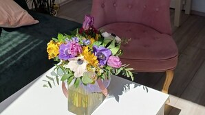 Un salon avec un canapé rose, une table basse blanche agrémentée d’un arrangement floral, un canapé vert et une porte blanche portant l’inscription « SORTIE ».