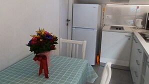 Une cuisine de taille réduite avec un puits de lumière, une table à manger recouverte d’une nappe à carreaux et un bouquet de fleurs.