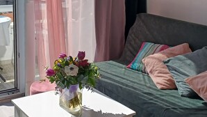 Une chambre moderne avec un lit, une table blanche ornée d’un vase de fleurs et une chaise rose.