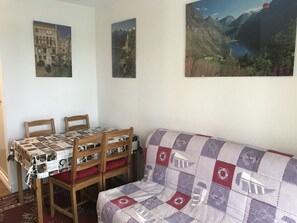 A dining area with a table covered by a newspaper print tablecloth, wooden chairs, and a sofa with a patchwork quilt.