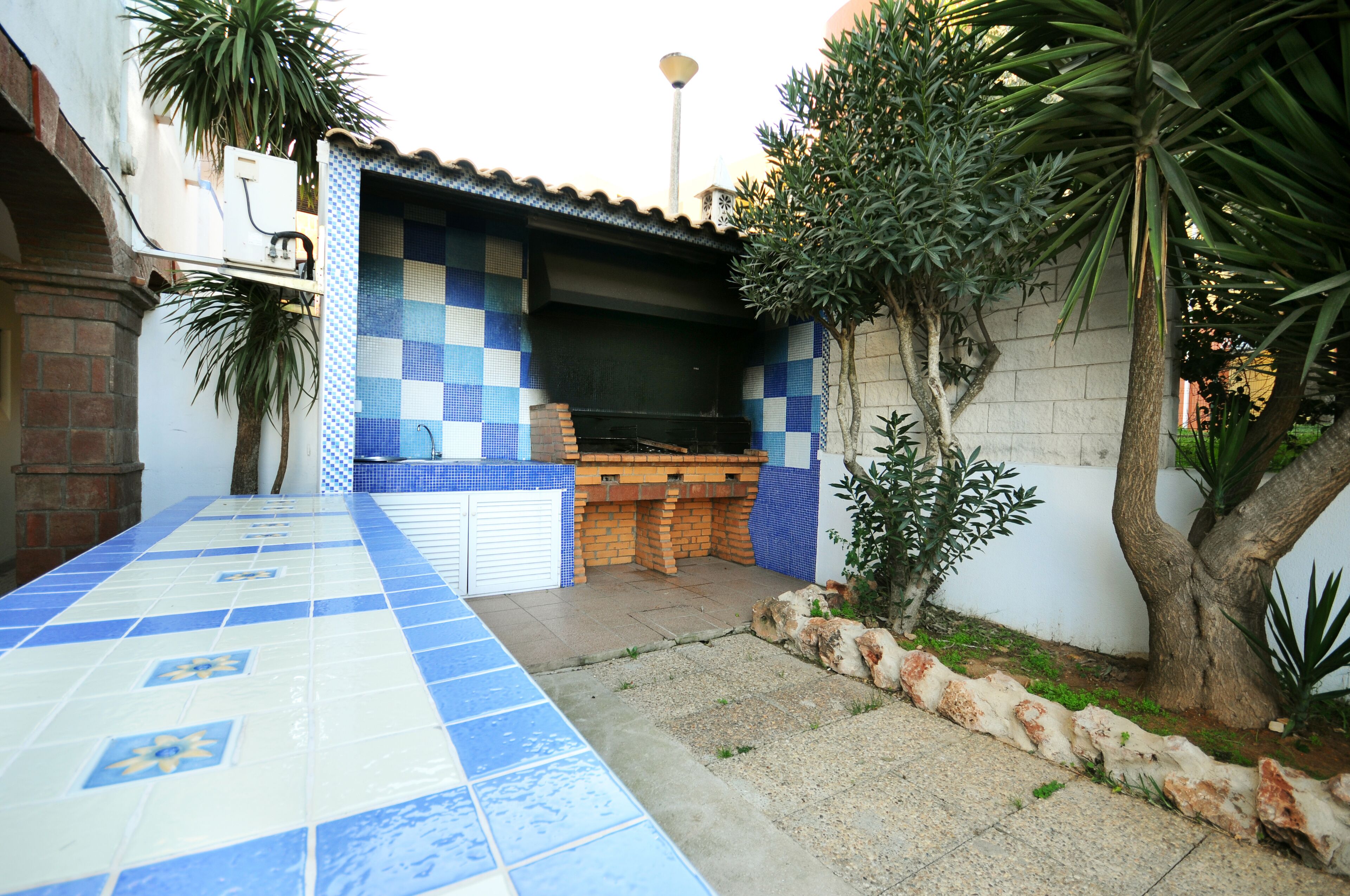A courtyard with a tiled patio, a brick barbecue area, and a tree.