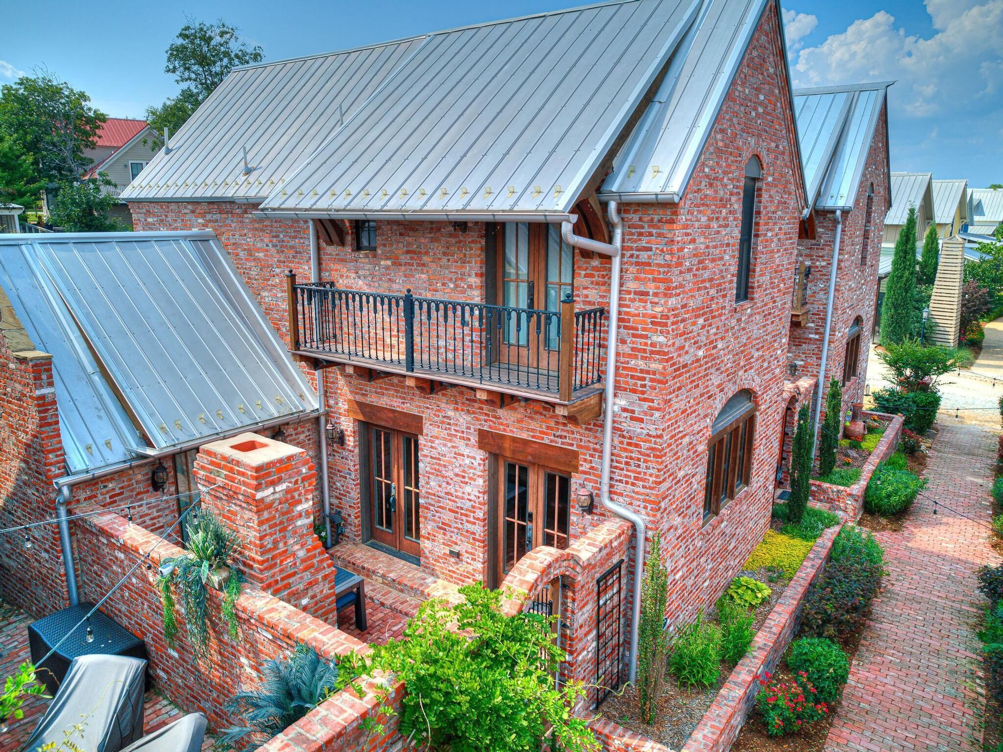 A two-story brick house with a balcony, a covered patio, and a brick pathway.