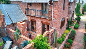 Ein zweistöckiges Backsteinhhaus mit Balkon, überdachter Terrasse und Pflasterweg.