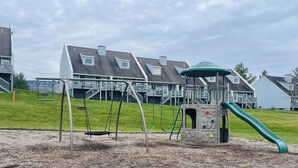 Un parque infantil con columpios y un tobogán, con edificios residenciales al fondo.