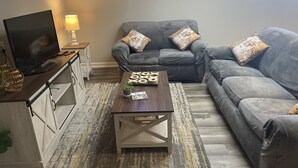 Una sala de estar con un sofá gris, una mesa de centro de madera, un televisor y una lámpara.