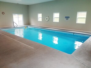 An indoor swimming pool with clear water, a lifebuoy, and a notice sign on the wall.