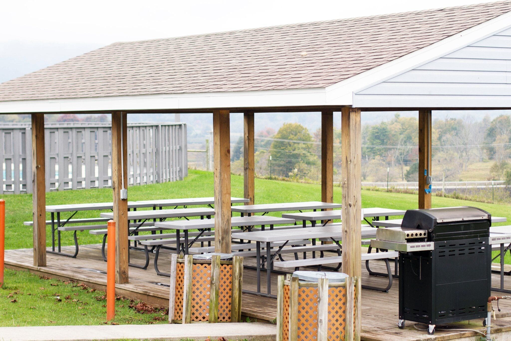 An outdoor covered picnic area with multiple picnic tables and a barbecue grill.