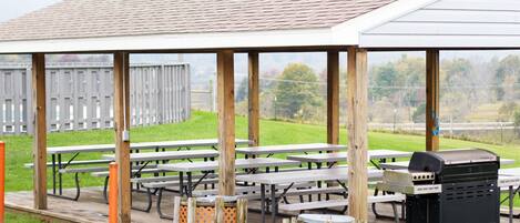 An outdoor covered picnic area with multiple picnic tables and a barbecue grill.