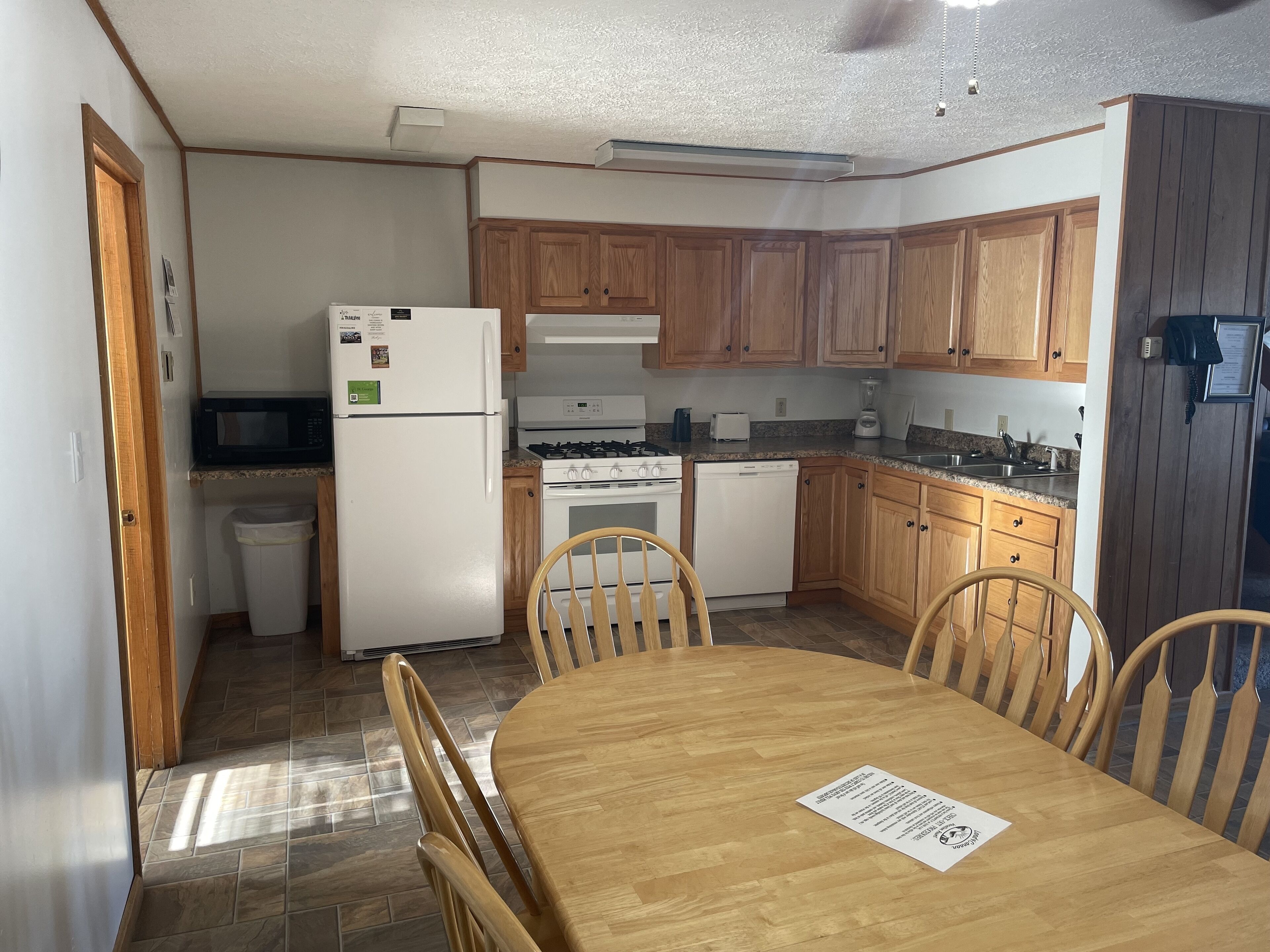 Una cocina compacta con armarios de madera, un refrigerador, estufa, microondas y una mesa de comedor con sillas.