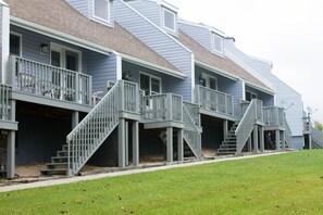 A row of townhouses with external staircases leading to the entrance, a grassy front yard, and a clear sky.